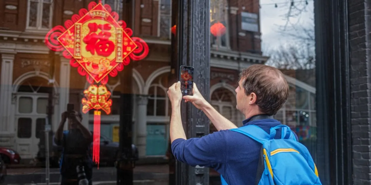 A man taking a photo of a Chinese lantern in a window reflection